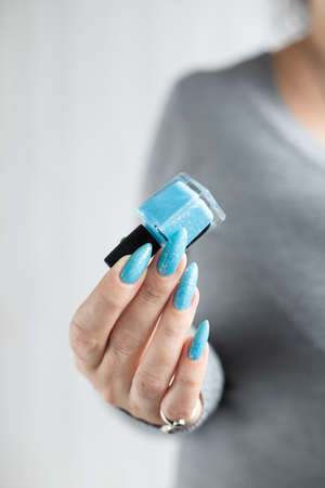 Female hand with long nails and light blue manicure with bottles of nail polishの写真素材