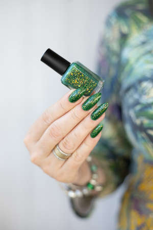 Female hand with long nails and bright green manicure with bottles of nail polishの写真素材