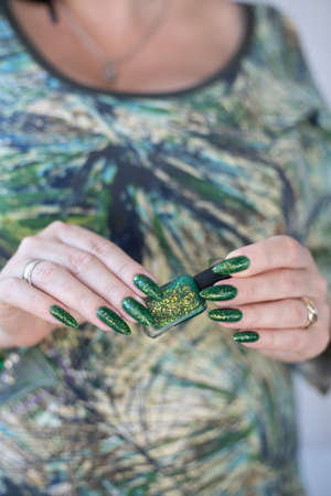 Female hand with long nails and bright green manicure with bottles of nail polishの写真素材