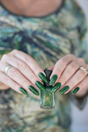 Female hand with long nails and bright green manicure with bottles of nail polishの写真素材
