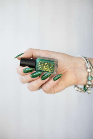 Female hand with long nails and bright green manicure with bottles of nail polish