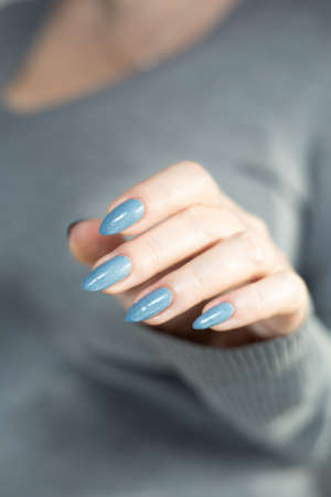Woman's beautiful hand with long nails and light blue manicure with bottles of nail polishの写真素材