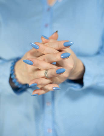 Woman's beautiful hand with long nails and light blue manicure with bottles of nail polish