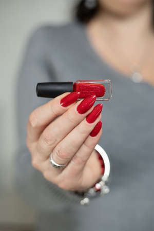 Female hand with long nails and a bottle with red nail polishの写真素材