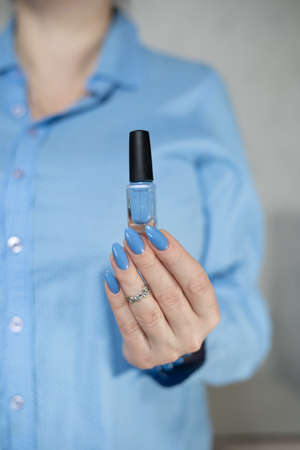 Woman's beautiful hand with long nails and light blue manicure with bottles of nail polishの写真素材