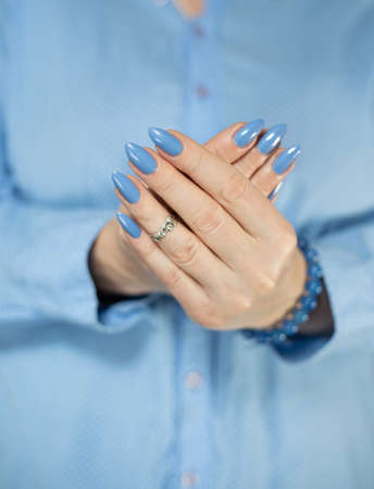 Woman's beautiful hand with long nails and light blue manicure with bottles of nail polishの写真素材