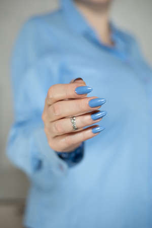 Woman's beautiful hand with long nails and light blue manicure with bottles of nail polishの写真素材