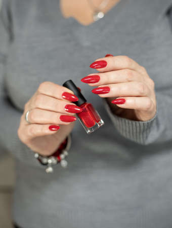 Female hand with long nails and a bottle with red nail polish