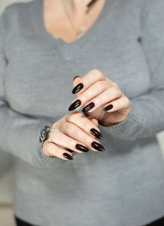 Female hand with long nails and gray black manicure with bottles of nail polishの写真素材
