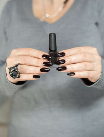 Female hand with long nails and gray black manicure with bottles of nail polishの写真素材