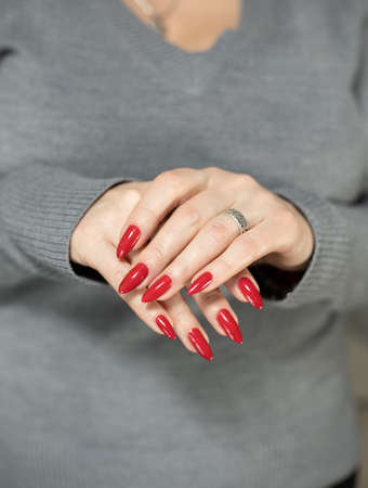Woman's hands with long nails and a bottle of red nail polishの写真素材