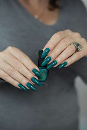 Female hand with long nails and light blue turquoise manicure with bottles of nail polish