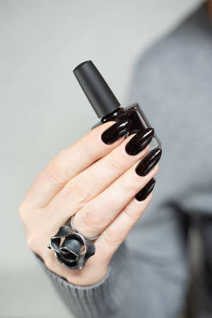 Female hand with long nails and gray black manicure with bottles of nail polishの写真素材