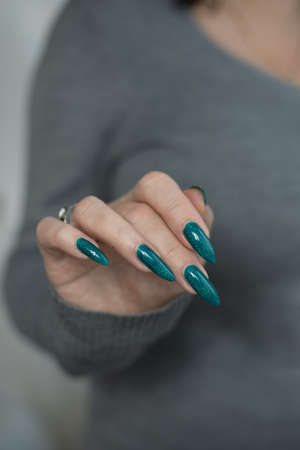 Female hand with long nails and light blue turquoise manicure with bottles of nail polish