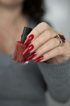 Woman hand with long nails and a bottle of dark red nail polishの写真素材