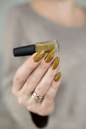 Female hand with long nails and a bottle of bronze golden nail polishの写真素材