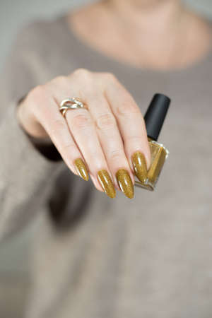 Female hand with long nails and a bottle of bronze golden nail polishの写真素材