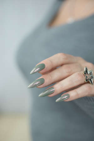Female hand with long nails and gray green manicure with bottles of nail polishの写真素材