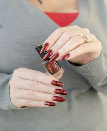 Woman hand with long nails and a bottle of dark red nail polishの写真素材