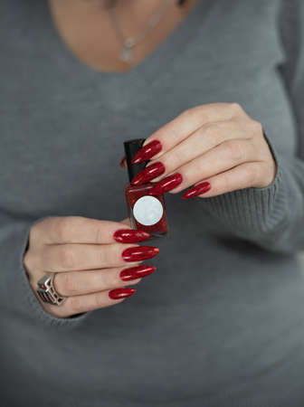 Woman hand with long nails and a bottle of dark red nail polish