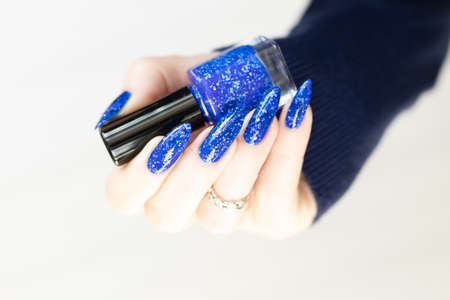 Female hand with long nails and bright blue manicure with bottles of nail polish