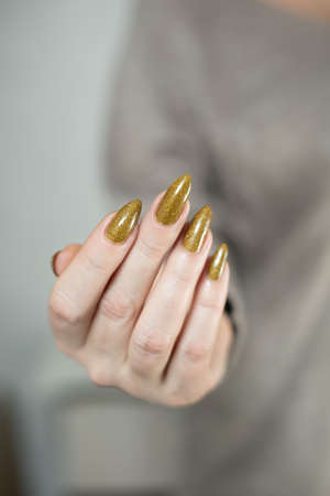 Female hand with long nails and a bottle of bronze golden nail polishの写真素材