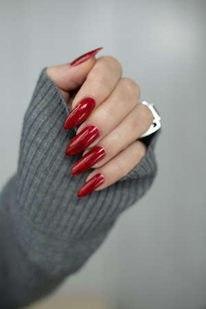 Woman hand with long nails and a bottle of dark red nail polishの写真素材