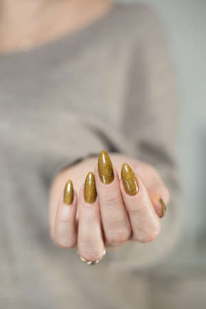 Female hand with long nails and a bottle of golden bronze brown nail polishの写真素材
