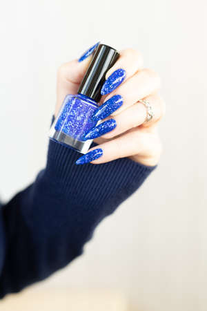 Female hand with long nails and bright blue manicure with bottles of nail polishの写真素材