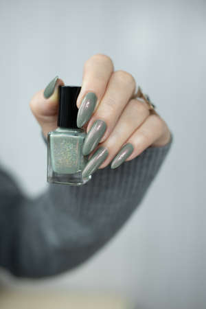 Female hand with long nails and gray green manicure with bottles of nail polishの写真素材