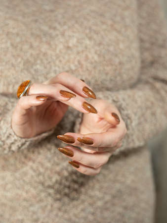 Female hand with long nails and a bottle of bronze golden nail polishの写真素材