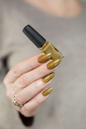 Female hand with long nails and a bottle of bronze golden nail polishの写真素材