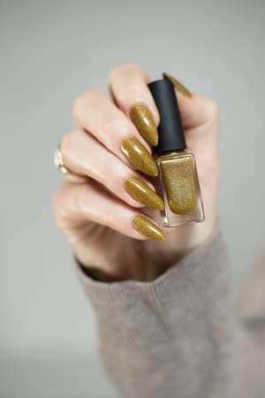 Female hand with long nails and a bottle of golden bronze brown nail polishの写真素材