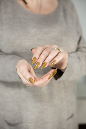 Female hand with long nails and a bottle of golden bronze brown nail polishの写真素材