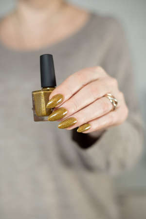 Female hand with long nails and a bottle of bright yellow green nail polishの写真素材