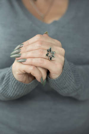 Female hand with long nails and gray green manicure with bottles of nail polish