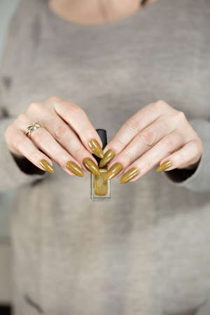 Female hand with long nails and a bottle of golden bronze brown nail polishの写真素材