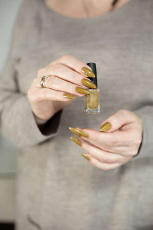 Female hand with long nails and a bottle of golden bronze brown nail polish