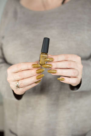 Female hand with long nails and a bottle of bright yellow green nail polishの写真素材