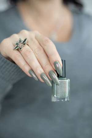 Female hand with long nails and gray green manicure with bottles of nail polishの写真素材