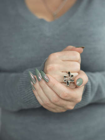 Female hand with long nails and gray green manicure with bottles of nail polish