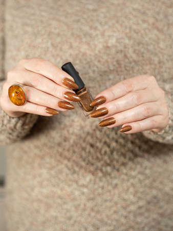 Female hand with long nails and a bottle of golden bronze brown nail polishの写真素材