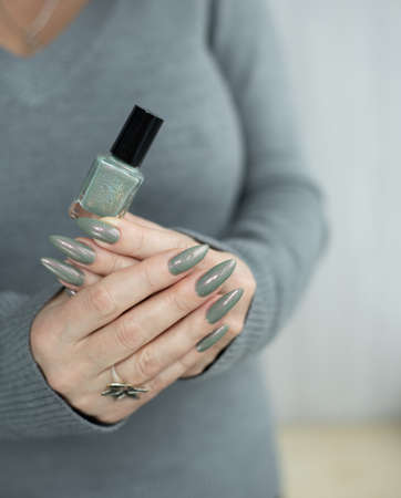 Female hand with long nails and gray green manicure with bottles of nail polishの写真素材