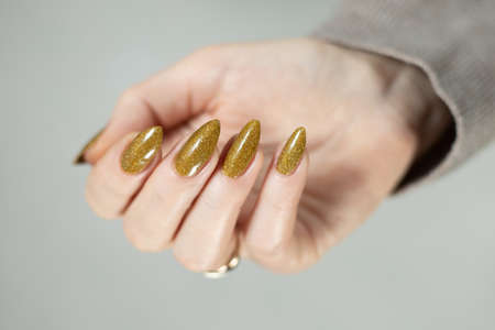 Female hand with long nails and a bottle of bright yellow green nail polishの写真素材