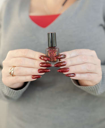 Female hand with long nails and a red manicure holds a bottle of nail polishの写真素材