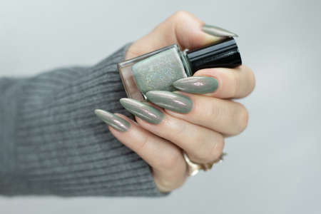 Female hand with long nails and bright green manicure with bottles of nail polishの写真素材