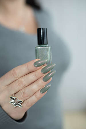 Female hand with long nails and bright green manicure with bottles of nail polishの写真素材