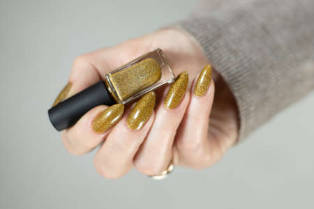 Female hand with long nails and a bottle of bright yellow green nail polishの写真素材