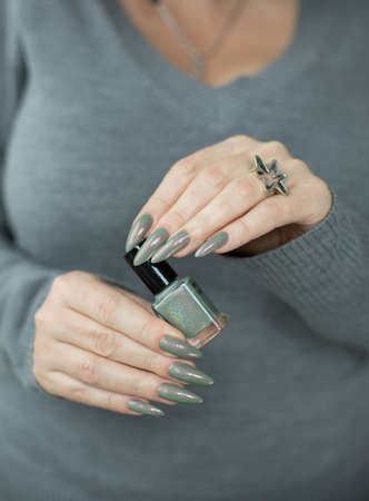 Female hand with long nails and gray green manicure with bottles of nail polishの写真素材