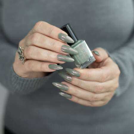 Female hand with long nails and gray green manicure with bottles of nail polishの写真素材